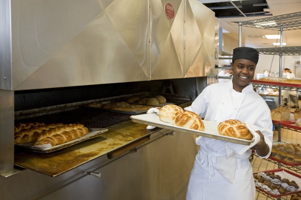 A student holds fresh loaves on a cookie sheet. 
