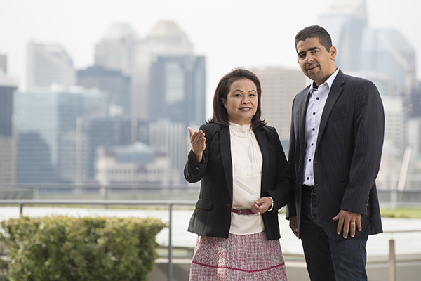 A man and woman in business attire look at the camera while having a discussion outdoors. The Calgary skyline can be seen behind them.