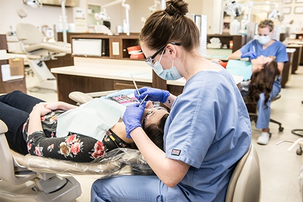 A dental assisting student performing dental check up on a patient