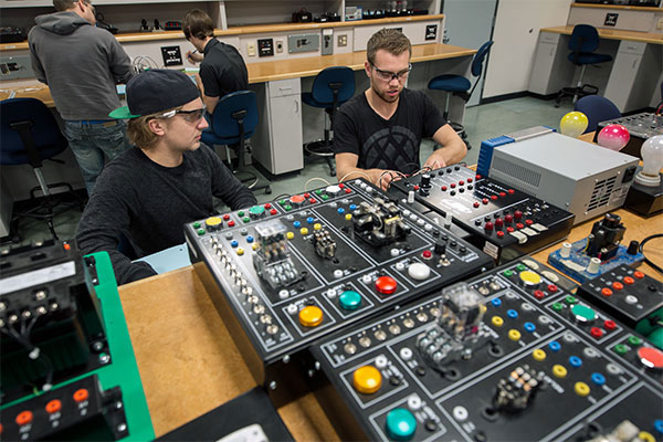 Two male students sit in a SAIT lab working with a large electrical board.