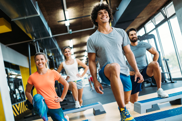 A group of men and women in workout gear do lunges in a fitness class.