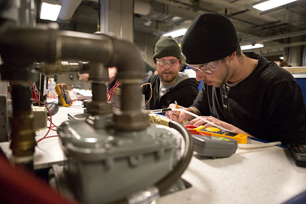 Two students wearing safety glasses perform propane metering tests in a SAIT lab.