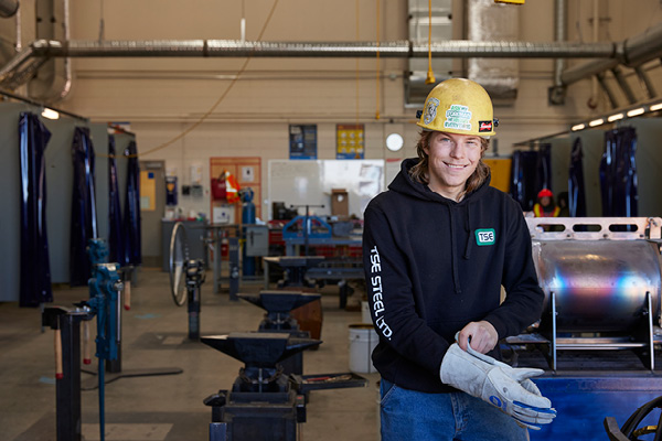 Student wearinga hardhat and gloves smiles at the camera
