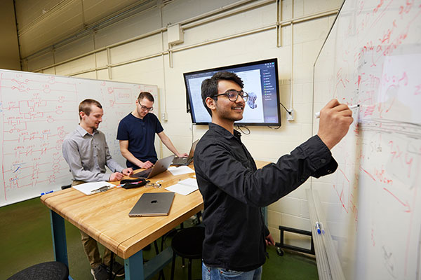 Three mechanical engineering students work together to map out a design on a whiteboard.