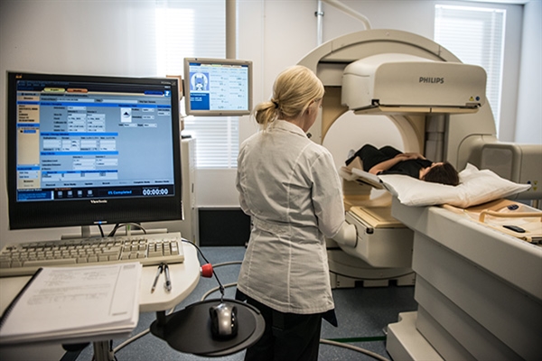 A student oversees a patient receiving a mock CT scan. The scan information can be seen on a computer monitor in the foreground. 