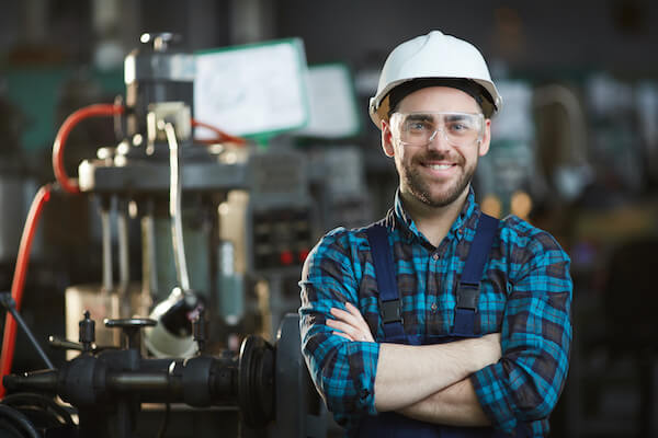 A pre-employment industrial mechanic student wearing a white hardhat and safety overalls smiles at the camera.