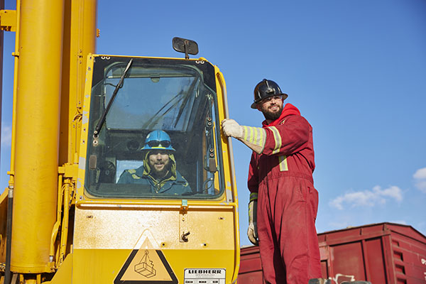 Two men in safety gear operating a crane and smiling