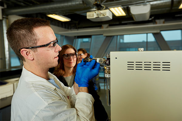 Three students wearing safety glasses and lab coats analyze water samples using specialized equipment in a SAIT lab.