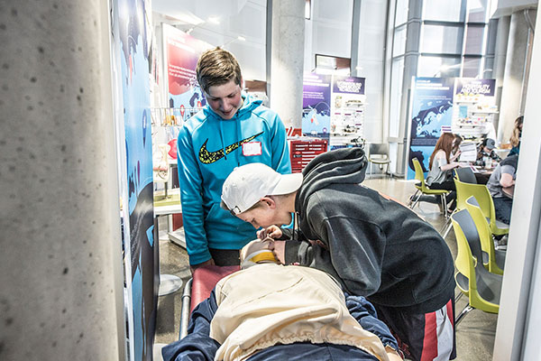 Two male high school students practice CPR on a dummy.